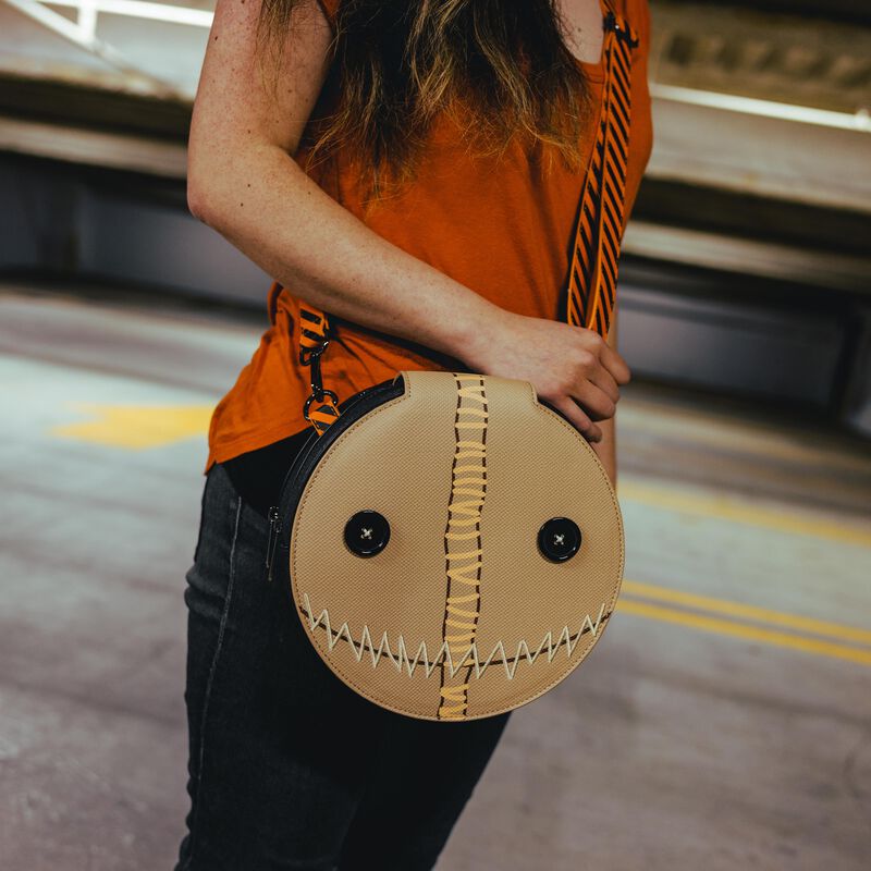 Image of woman wearing the Trick 'r Treat Sam Pumpkin Crossbody with the front flap closed, showing Sam's burlap smiling face of his costume